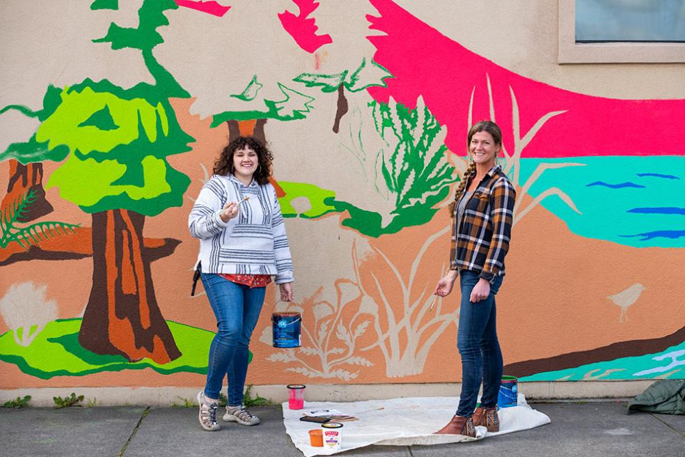 Caroline Voorhees (left), student teacher and Art Education alumna, and Redwood Coast Montessori High School art teacher Saha Lyth (left), working on the school mural.