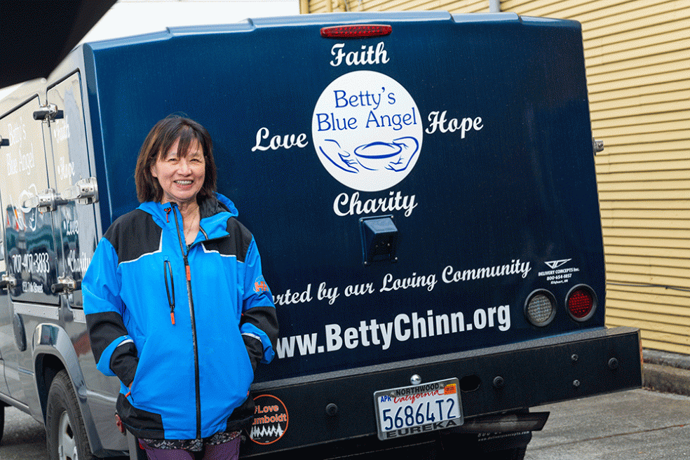 Betty Chinns smiles as she stands at the bumper of a Betty's Blue Angel truck