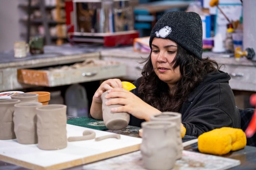 A photo of a student sponging clay mugs to be identical.