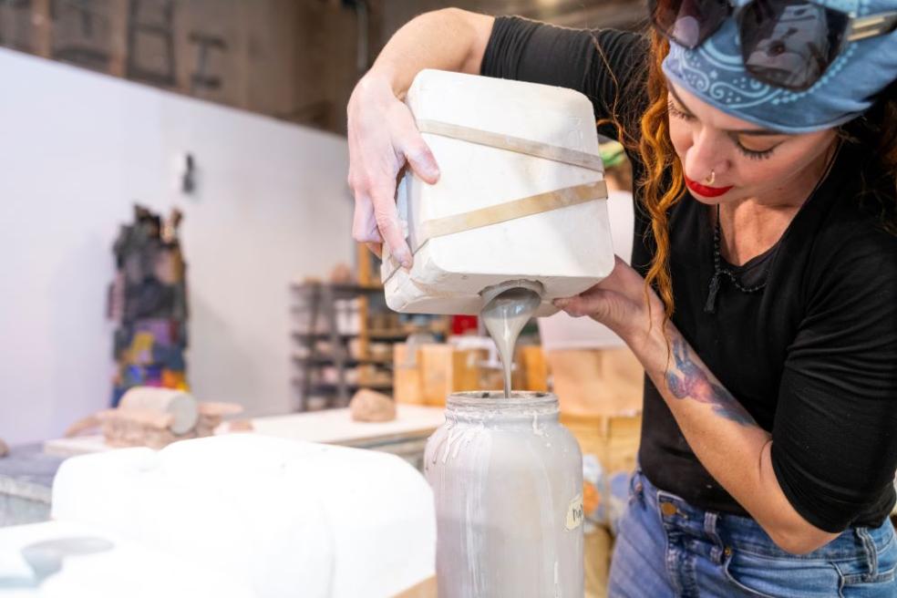 A photo of a student pouring silicone to create a mold for a ceramic mug.