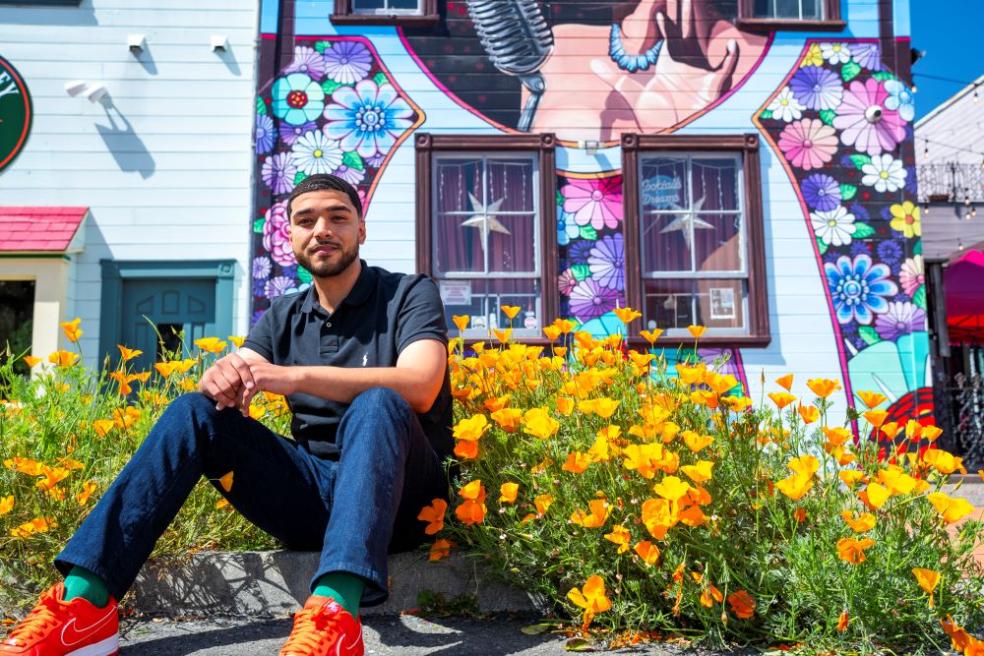 A photo of Dillon Harp, CSU Trustees Scholar, sitting by a bed of flowers. 