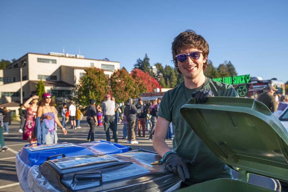 student smiling and standing next to waste bins, opening a lid to one can