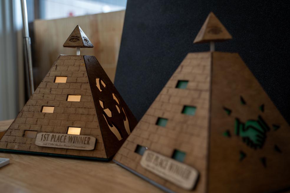 The "Pyramid of Business & Economics" trophy will be awarded to the winner of the Business, Economics, and Hospitality Management category. It features handshake and recycling symbols, symbolizing community and sustainability.