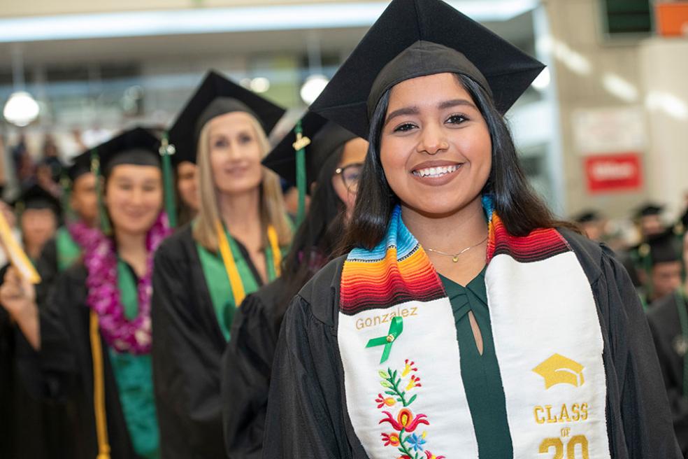 A female graduate smiling, dressed in a black cap and gown with a Hispanic stole that reads "Gonzalez." 