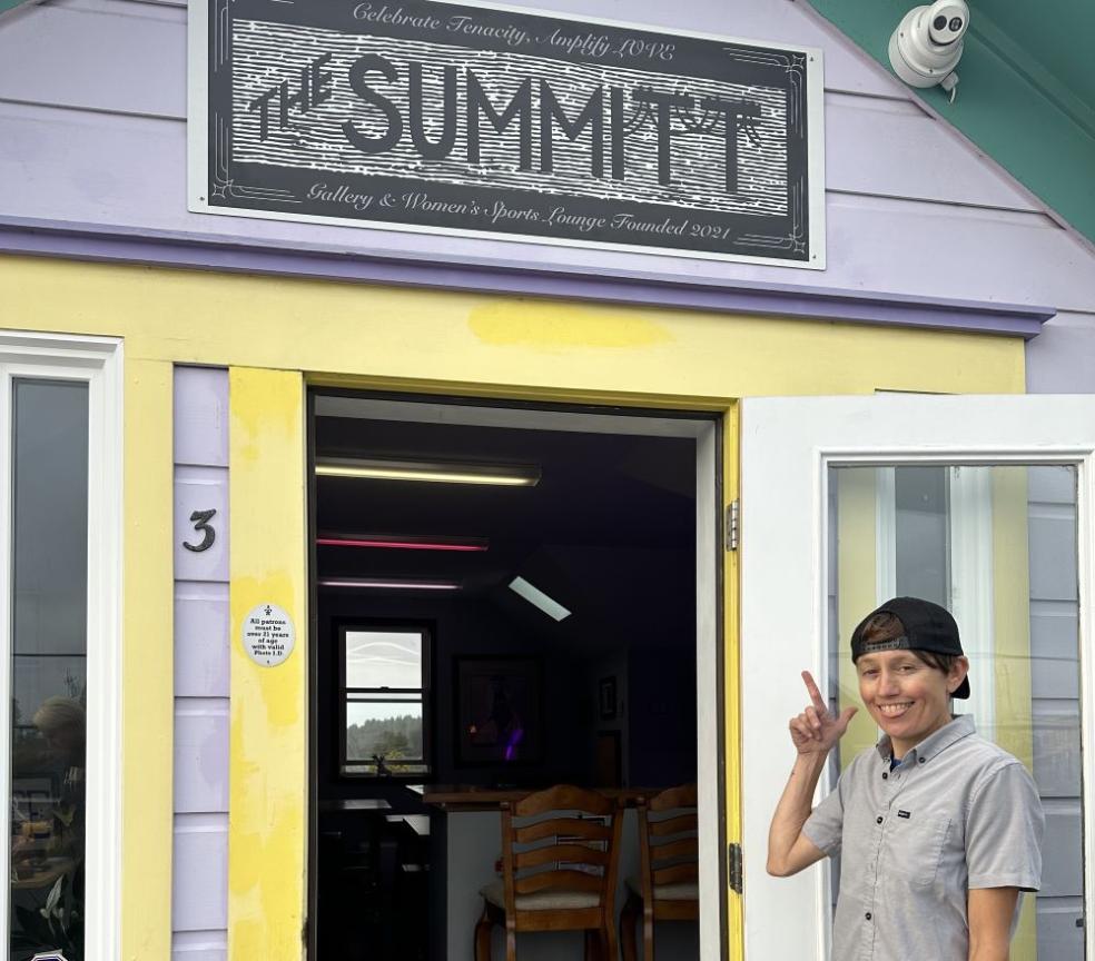 A photo of Michelle Cartier pointing at The Summitt sign at the entrance of The Summitt