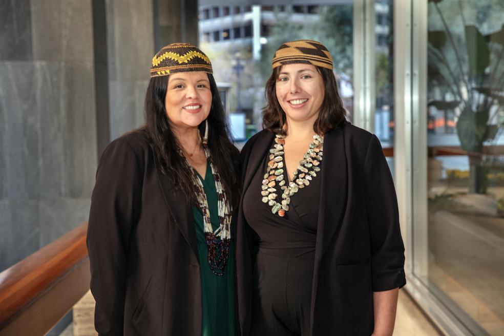 Professors Reed (right) and Risling Baldy (left) standing side by side and smiling, wearing native headpieces and necklaces. 