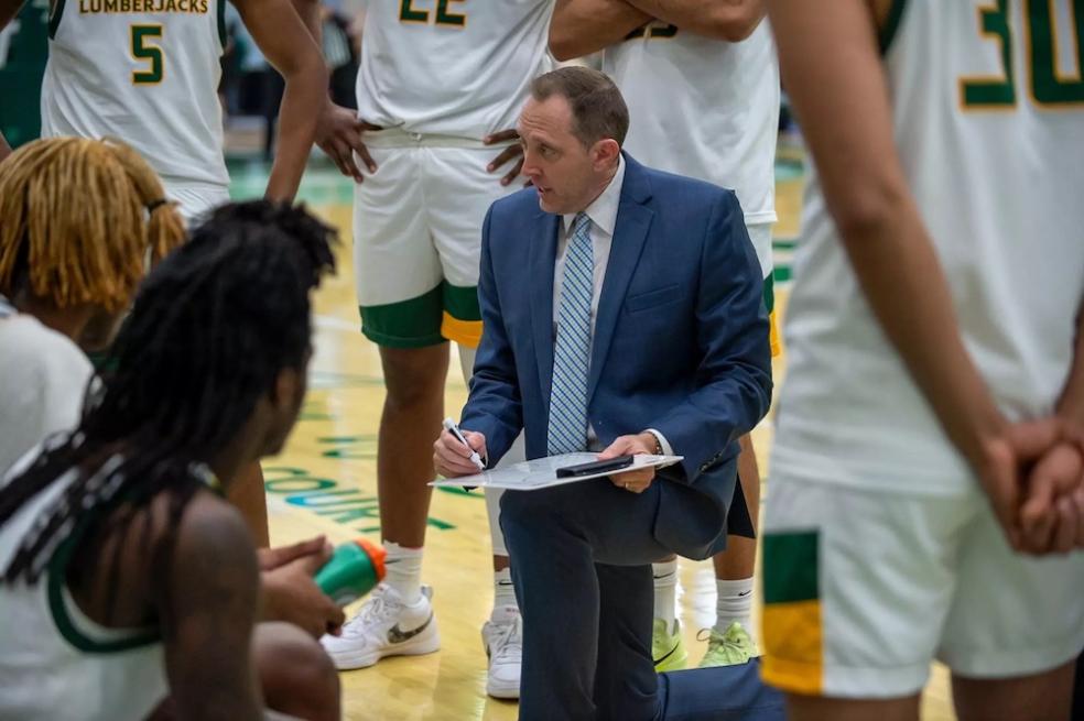 men's basketball coach down on one knee drawing on a whiteboard 