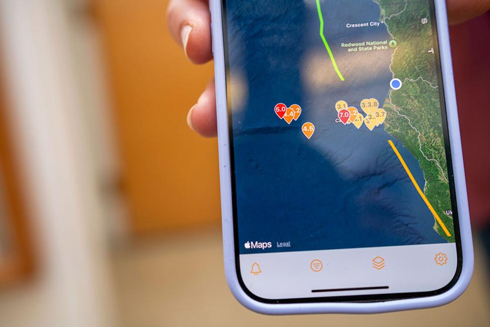 someone holding up their iphone, the screen shows a map of recent earthquakes off the coast of Northern California 