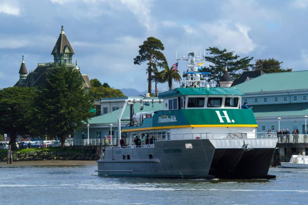 A photo of the R/V North Wind docked in front of the Humboldt Bay Aquatic Center with the Carson Mansion in the background.