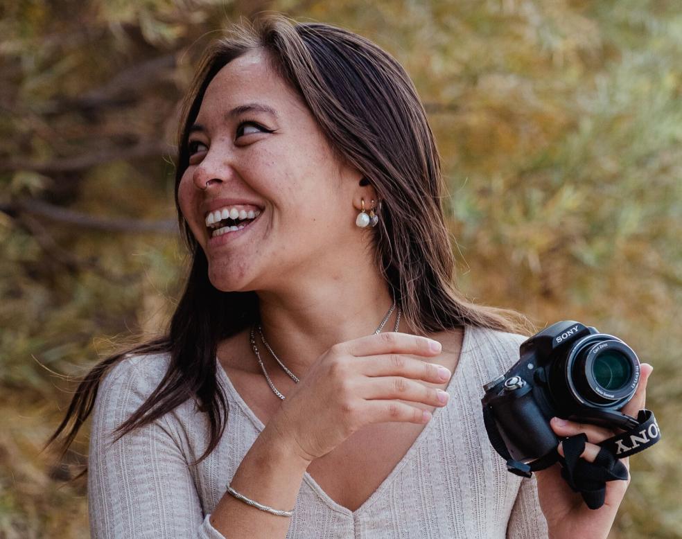A photo of Eva Sideris smiling and looking right while holding a camera.