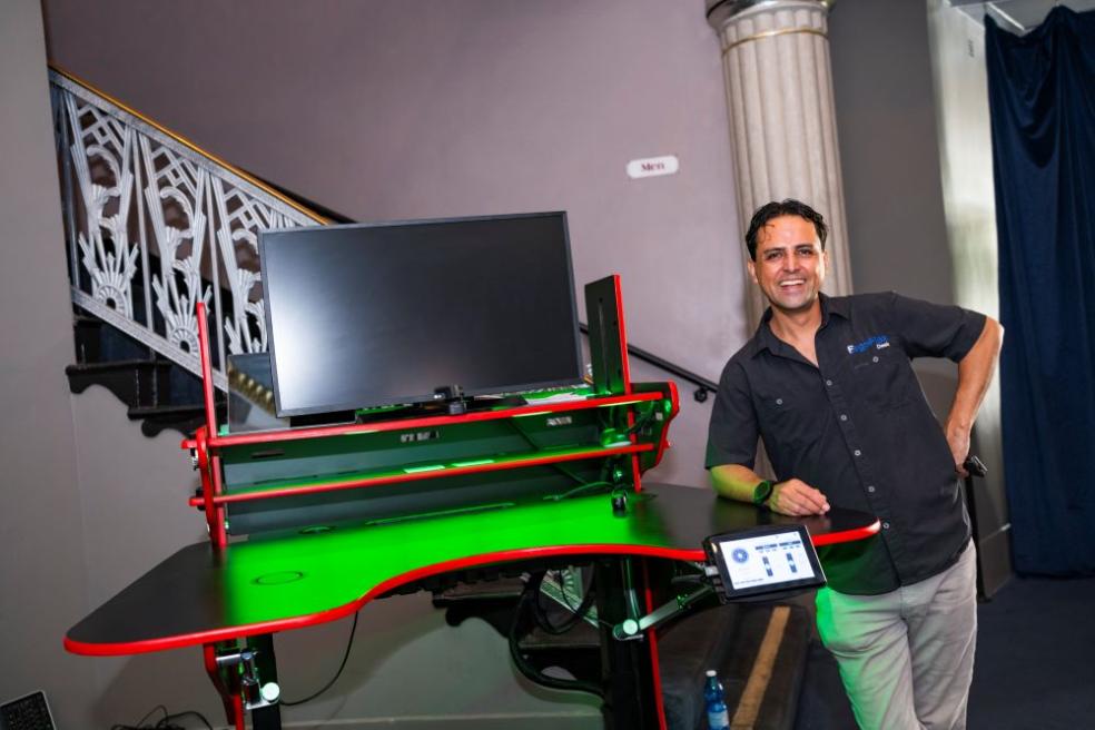 A photo of Vico Hernandez standing next to his innovative ErgoFlex Desk at regional commencement.