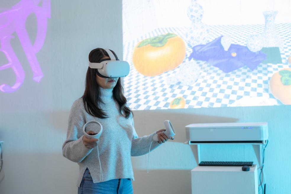 a female standing with a VR set on their head and an image of a table setting projected on the wall behind them.