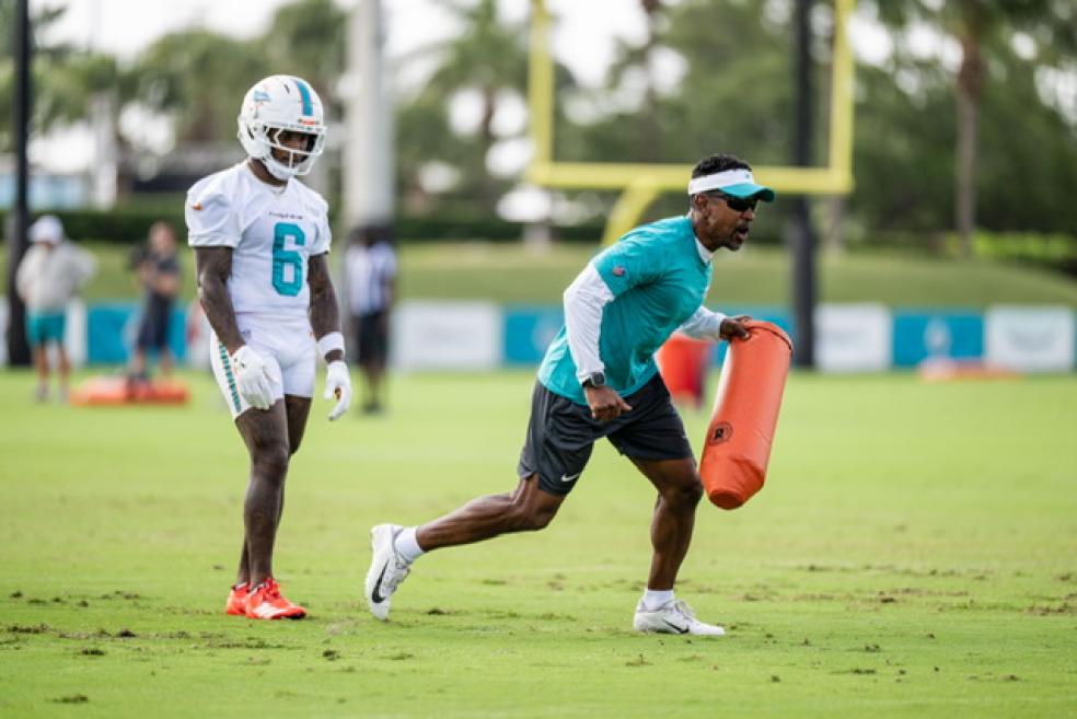 A photo of Robert Prince running with a football pylon and a Miami Dolphins player in full practice gear during a training session.