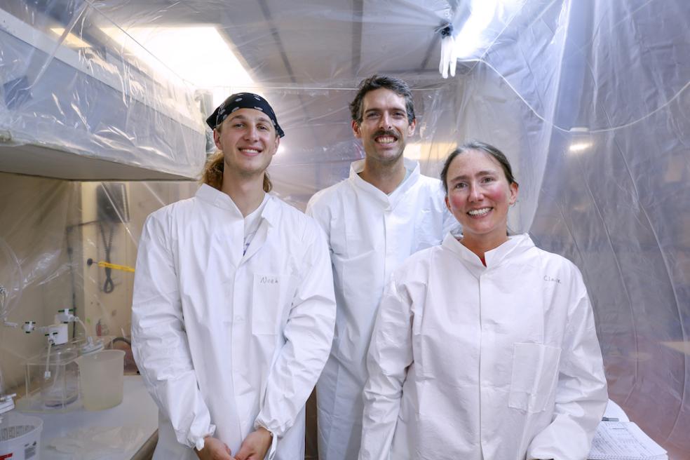 From left to right: Noah Schuhmann, Ralph Till, and Claire Till stand inside the “bubble,” a cleanroom they constructed onboard the research vessel to prevent potential contamination of the seawater samples they collected. Photo from Karina Vivanco.