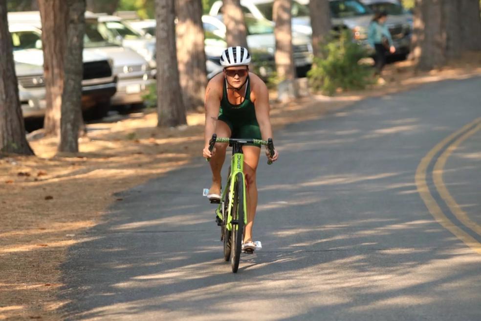 athelete riding bike on paved pathway with trees and cars in the background
