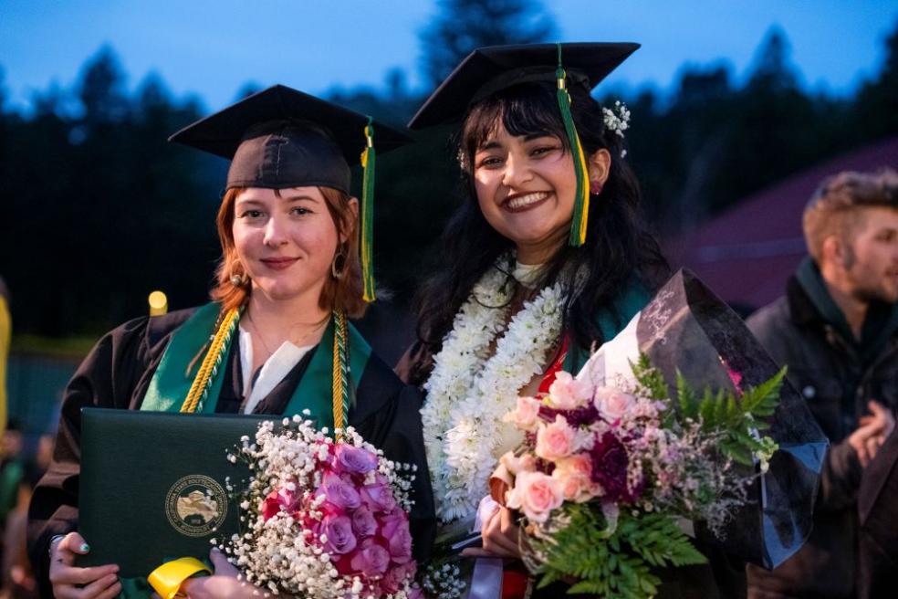 A photo of two graduates posing for a photo outside of the Kinesiology & Athletics building after Fall Commencement.