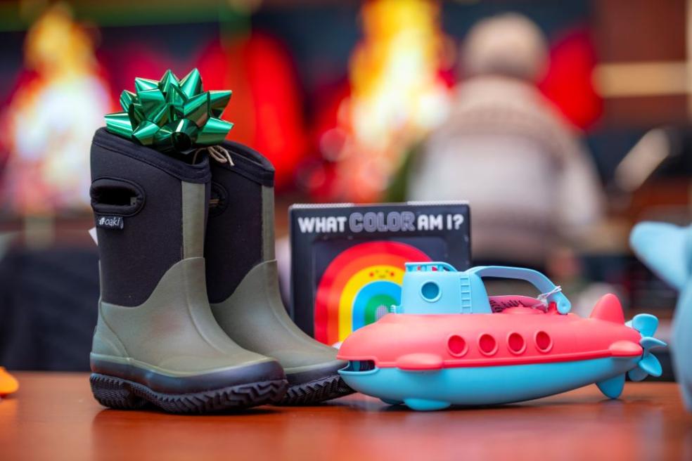 A photo of a pair of rainboots and toys sitting on a table waiting to be wrapped into Winter Wishes gifts. 