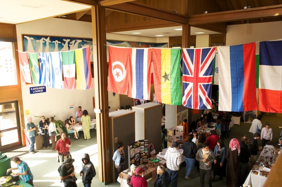 Flags from several different nations hang above several people visiting the IEW's international cultural festival 