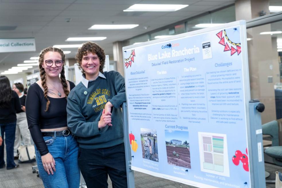 A photo of two students standing in front of their poster presentation in the Library during ideaFest in 2025. 