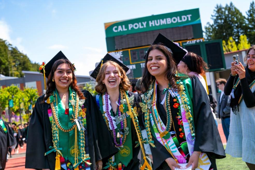 A photo of three grads at spring Commencement in the redwood bowl. 