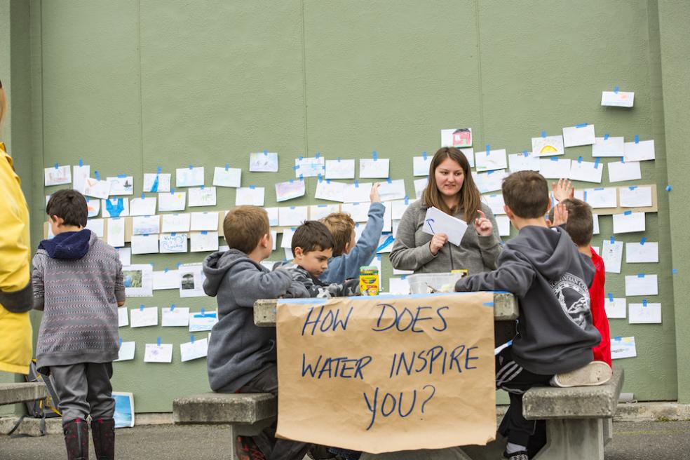 children sitting at a bench with a sign attached to it that reads, "how does water inspire you?"