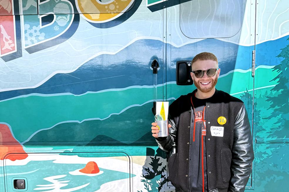 A photo of Carlo Solis standing in front of the mobile alumni center holding the Cal Poly Humboldt koozie during the Forever Humboldt at the San Francisco Giants game. 