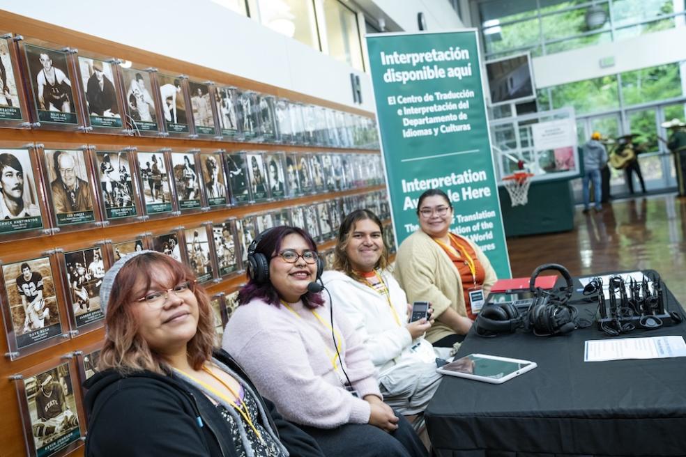 Four people sitting at a table with a banner behind them that describes the center for Translation & Interpretation services