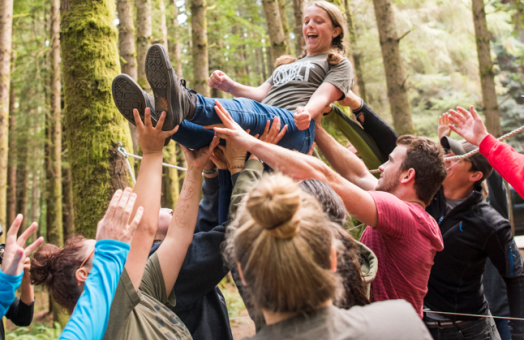 A photo of Cal Poly Humboldt students holding up another student in the forest.