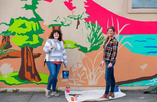 Caroline Voorhees (left), student teacher and Art Education alumna, and Redwood Coast Montessori High School art teacher Saha Lyth (left), working on the school mural. 