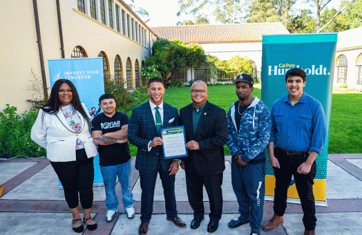 Improve Your Tomorrow CEO (center left) and Cal Poly Humboldt President Tom Jackson, Jr. (center right) stand with students at a signing ceremony. 