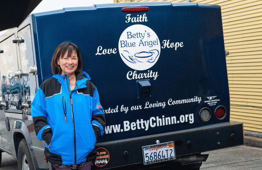 Betty Chinns smiles as she stands at the bumper of a Betty's Blue Angel truck