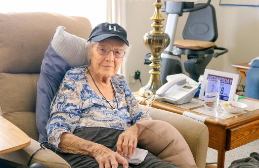 A photo of 102-year-old alum Sarah Franklin sitting on a chair wearing a Humboldt &quot;H dot&quot; baseball cap. 