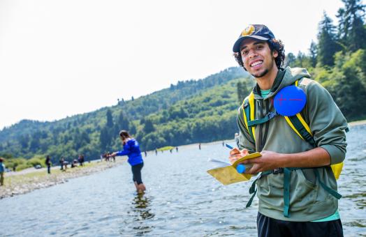 A photo of a student standing in the Klamath River taking notes. 