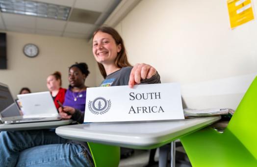 A photo of a student holding a sign with South Africa written on it to represent the country in Model UN. 