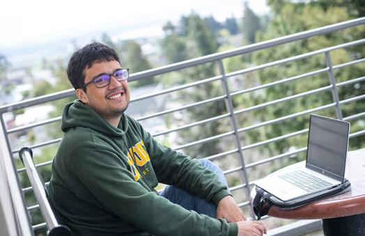 Matias Solorzano sits next to his lap on a balcony with trees in the background