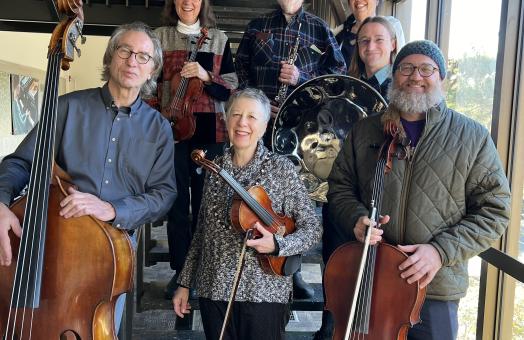 The concert's musicians standing on a staircase with their instruments in hand and smiking. 