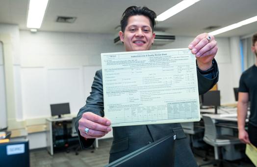 student smiling and holding up a tax form for the camera
