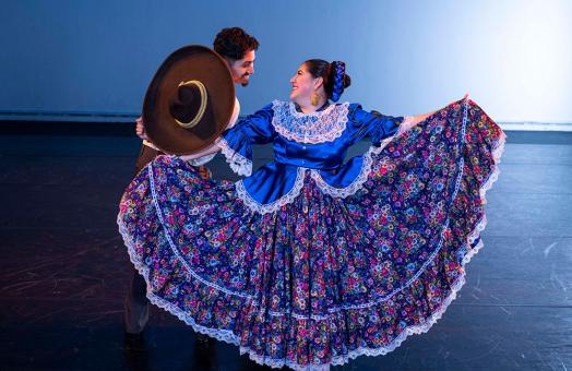 male and female folklorico dancers looking at teach other, male is holding up a hat and female is spreading her colorful floral skirt. 