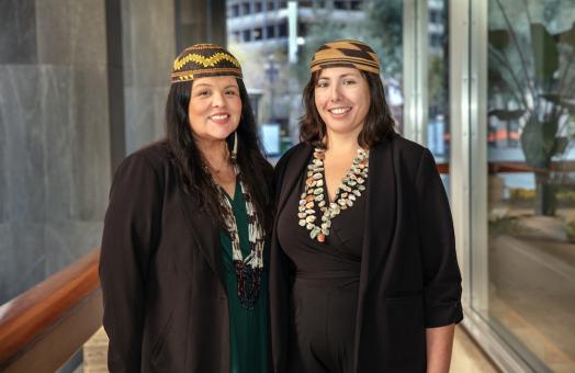 Professors Reed (right) and Risling Baldy (left) standing side by side and smiling, wearing native headpieces and necklaces. 