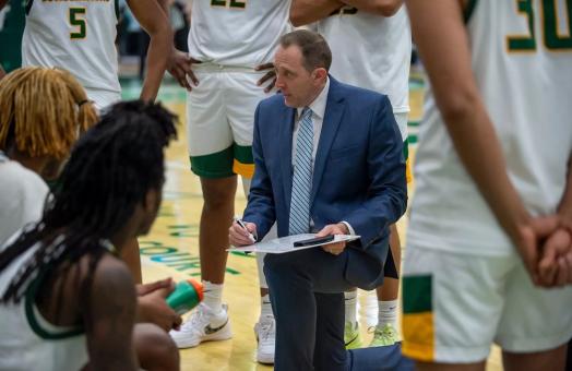 men's basketball coach down on one knee drawing on a whiteboard 