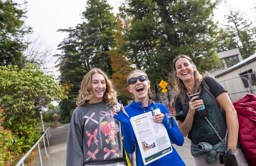 A photo of three women; one is a prospective student holding a rock in one hand and an informational booklet about the majors she can study at Cal Poly Humboldt during a University Preview event.