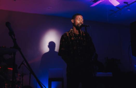 A photo of musician Dre-T on stage singing into a microphone with a spotlight.