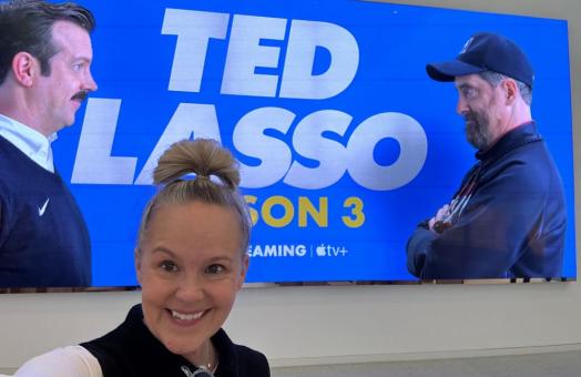 A photo of Leesa Coble in front of a poster for Ted Lasso