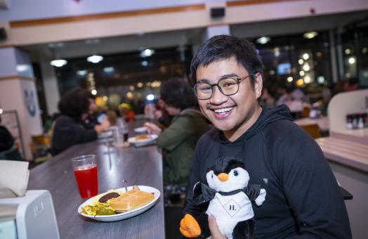 Student smiling with a plate in food in front of him and holding a build-a-bear
