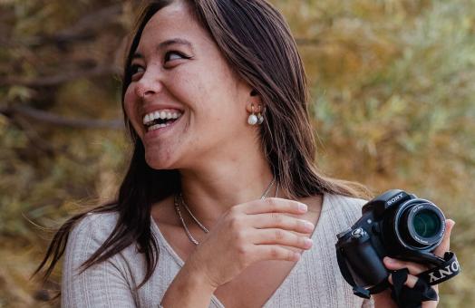 A photo of Eva Sideris smiling and looking right while holding a camera. 