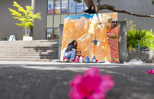 Two students and Professor James Woglom painting a large mural outside on the Art quad. 