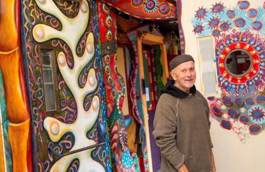 A photo of artist David White posing in front of the art hallway he created.