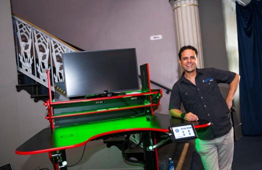 A photo of Vico Hernandez standing next to his innovative ErgoFlex Desk at regional commencement.