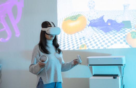 a female standing with a VR set on their head and an image of a table setting projected on the wall behind them. 