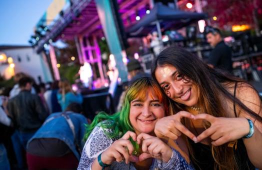 A photo of two students shaping their hands into the shape of hearts in front of the stage at Lumberjack Weekend 2024. 